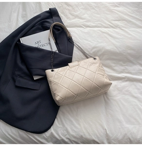 Detail of cream quilted shoulder bag with silver chain strap on a white background