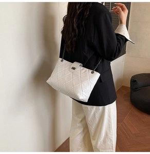 Close-up of white quilted chain shoulder bag with metal turn-lock on a model