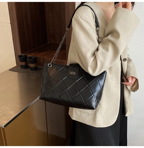 Detail of classic black quilted tote bag with metal chain strap and twist-lock closure