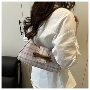 Detail of checkered baguette bag with brown leather bow accent worn by model