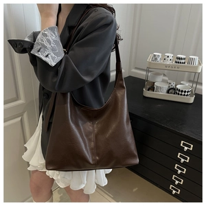 Detail of deep brown vintage faux leather tote bag worn by model in an urban office setting