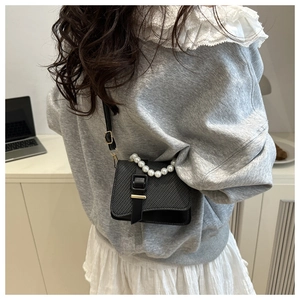 Detail of black textured mini crossbody bag featuring a large pearl handle and strap