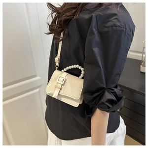 Detail of cream crossbody bag featuring woven texture and elegant pearl bead handle