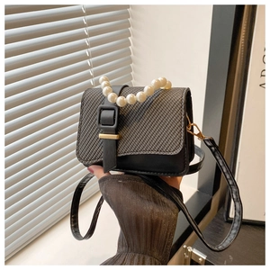 Detail of a black leather woven mini bag with pearl handle and gold square buckle
