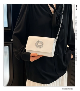 Detail of white leather crossbody bag featuring rhinestone buckle and silver chain strap