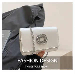 Close-up of the white leather crossbody bag featuring a sparkling crystal buckle detail