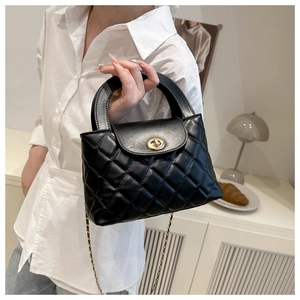 Classic black quilted bag detail featuring a gold twist-lock and metal chain strap on model