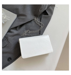 Detail of white leather crossbody bag with silver chain strap on grey fabric