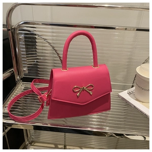 Detail of rose red mini crossbody bag with golden metal bow and textured PU leather