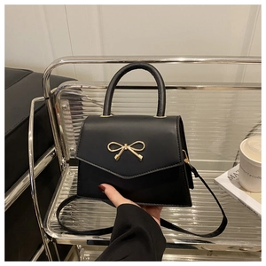 Close-up of black crossbody bag featuring a golden bow metal buckle and faux leather texture