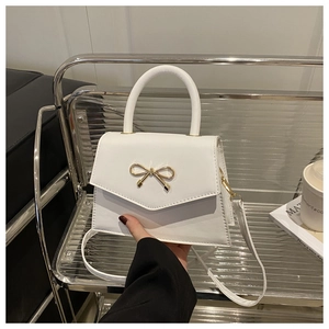 Detail of white PU leather mini handbag featuring a golden metal bow and rigid handle