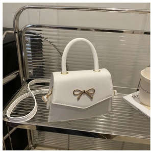 Detail of white mini crossbody bag featuring a golden bow buckle and fine leather texture