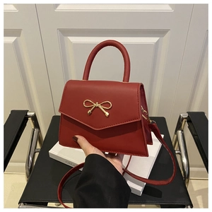 Detailed macro view of the red leather handbag featuring a refined golden bow metal buckle