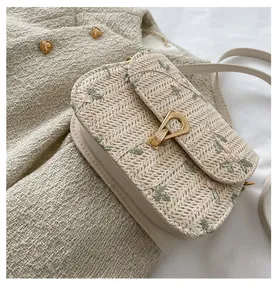 Detail of beige straw bag featuring green leaf embroidery and a golden metal clasp