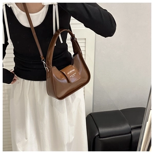 Detail of a brown glossy faux leather shoulder bag with white text and metal strap buckles