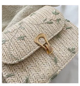 Detail of hand-woven straw bag featuring delicate floral embroidery and gold metal buckle