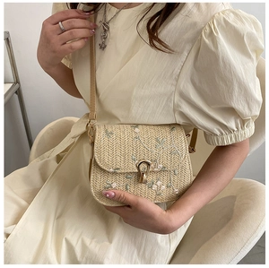 Detailed close-up of straw woven crossbody bag with delicate floral embroidery and gold lock