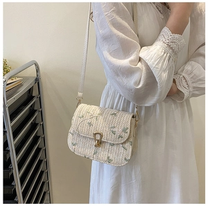 Détails de fleurs brodées roses et vertes sur un sac besace en paille crème