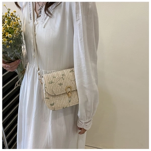 Straw saddle bag with green floral embroidery and gold clasp on a lace dress