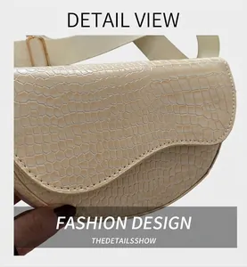 Close-up of cream saddle bag with crocodile texture and wide fabric strap on denim