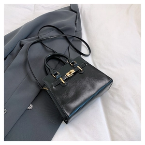 Detail of black glossy leather handbag with gold twist lock on a grey suit jacket