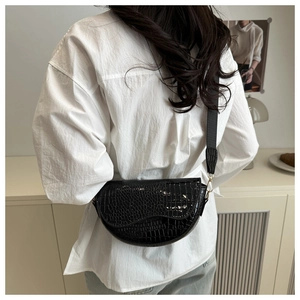 Detail of black faux crocodile leather saddle bag with wide adjustable strap on model