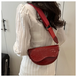 Detail of red crocodile pattern saddle bag with a wide nylon strap and gold hardware