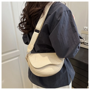 Detail of cream semi-circle saddle bag with crocodile pattern and wide knit strap