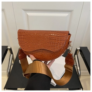 Detail of caramel brown saddle bag featuring glossy crocodile texture and wide strap