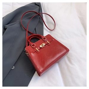 Detail of red textured faux leather handbag with gold twist lock on grey blazer