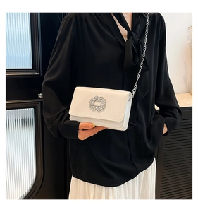 Detail of white leather shoulder bag with a sparkling round crystal buckle and silver chain