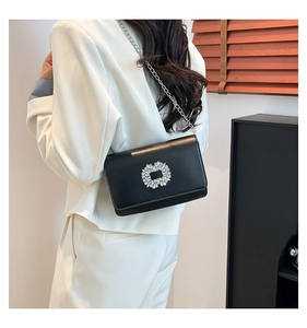 Close-up of black crossbody bag with large crystal buckle on a white suit model