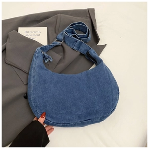 Detailed close-up of a large denim crescent shoulder bag with tassel and wide strap
