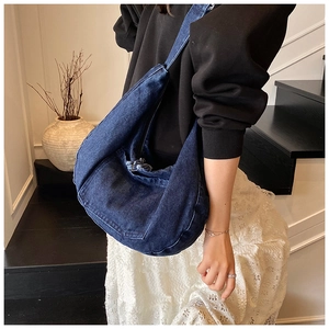 Close-up of deep blue denim crescent bag with frayed zipper detail and washed texture