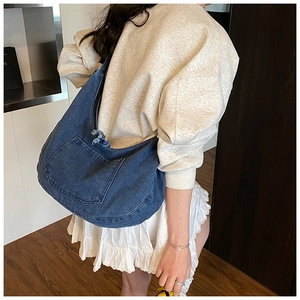 Detail of blue denim hobo bag featuring a front pocket and stylish woven drawstring