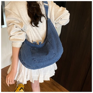 Detail of dark blue denim crossbody dumpling bag with a front pocket shown on a model