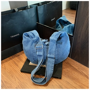 Detail of dark blue denim crescent bag featuring pocket stitching and fringe zipper pull
