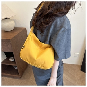 Detail of a bright yellow crossbody canvas bag with black tag shown on a female model