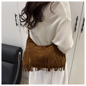 Brown faux suede hobo bag with long fringe tassels shown on shoulder of a model