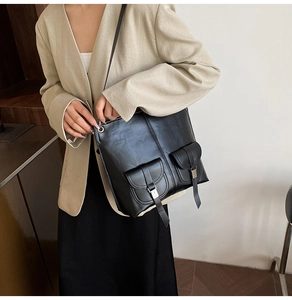 Detail of black faux leather tote bag with functional cargo pockets and metal buckles