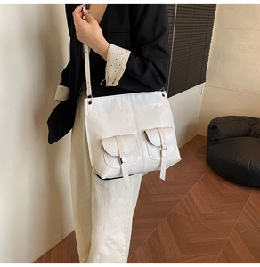 White leather shoulder bag with two flap pockets worn by a model in a minimalist setting
