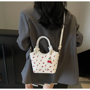 White cherry print bucket bag with adjustable strap worn as a crossbody shoulder bag
