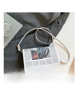 Close-up of vintage newspaper print on white leather envelope bag with gold hardware