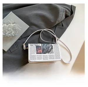 Detail of newspaper print shoulder bag featuring leather texture and gold metal ring strap