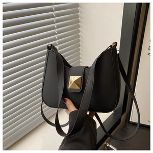 Detail of black minimalist square handbag featuring a prominent gold pyramid stud buckle
