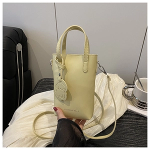 Detail of a creamy yellow mini phone bag with golden lettering and a dog charm accessory