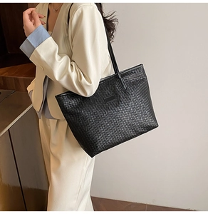 Detail of black woven tote bag with long shoulder straps on a person in white suit