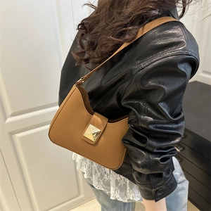 Minimalist brown leather shoulder bag with a gold pyramid stud on a model in a leather jacket