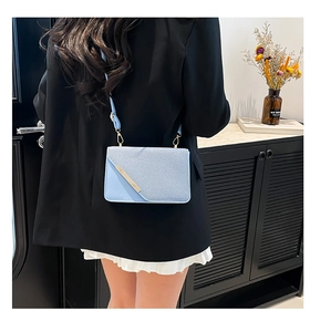 Détail d'un sac bandoulière bleu clair avec barre métallique dorée et rabat texturé