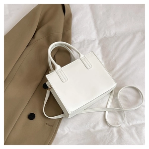 Detailed view of white minimalist handbag with adjustable strap on white linen background